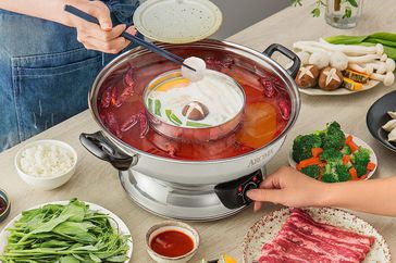 A person pulls food out of an Aroma Electric Hot Pot. 