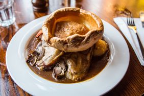 A plate of British roast dinner with roast lamb, Yorkshire pudding, roast carrots, potatoes, broccoli and gravy on a table in a pub