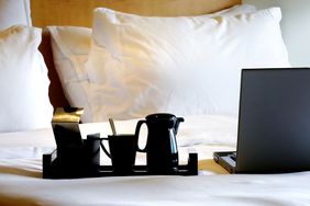 A hotel bed with a coffee tray and laptop