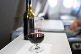 A bottle and a glass of red wine set on a tray table on a flight