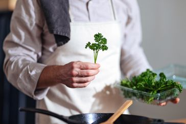 A chef stands in a home kitchen cooking with fresh herbs