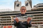 Chef holds up a fresh fish in front of a cruise ship