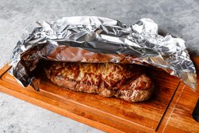 Grilled steak resting on wooden board covered with aluminum foil