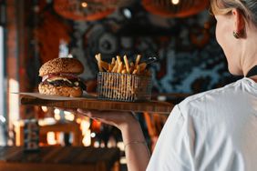 A server passes a table with a board of fries and a burger
